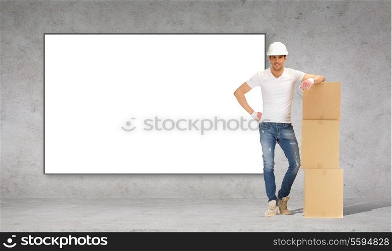 building, moving, advertisement and postal concept - smiling man in helmet and gloves with tower of cardboard boxes in tront of big billboard