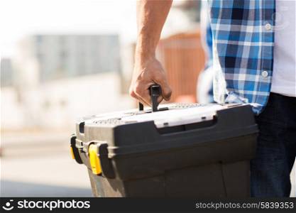 building, protective gear and people concept - close up of builder carrying toolbox at construction site