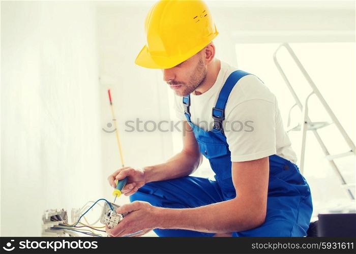 building, renovation, technology, electricity and people concept - builder with screwdriver fixing socket indoors