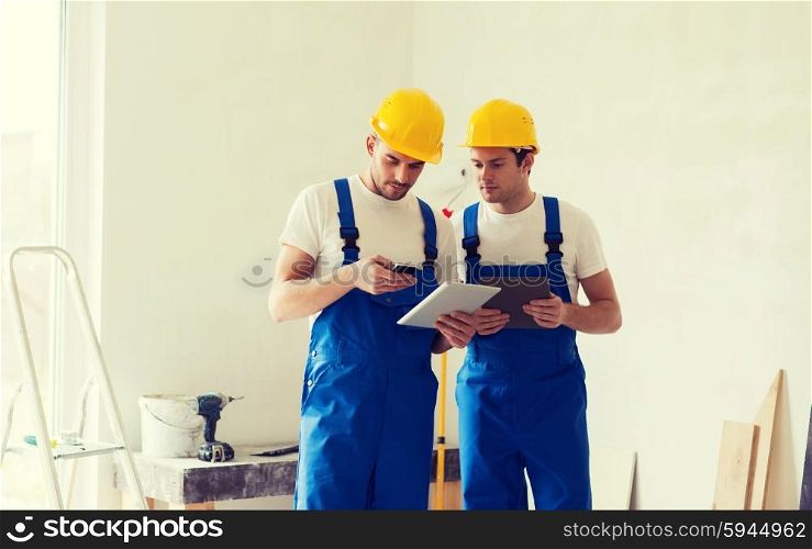building, renovation, technology, electricity and people concept - two builders with tablet pc computer and smartphone indoors