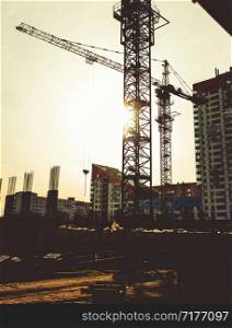 Building site with high-rise block under construction in an urban environment dominated by a large industrial crane silhouetted against sunset sky.. Building site with high-rise block under construction in an urban environment dominated by a large industrial crane silhouetted against sunset sky