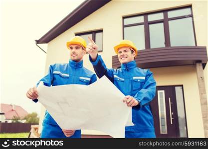 building, teamwork and people concept - group of smiling builders in hardhats and overalls with blueprint outdoors