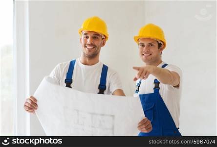 building, teamwork and people concept - group of smiling builders in hardhats with blueprint indoors