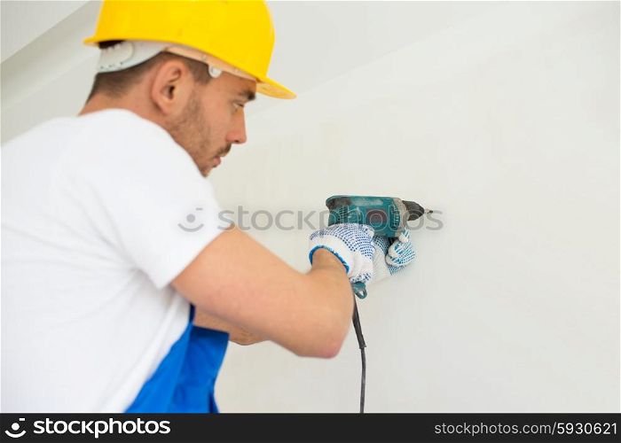building, teamwork, working equipment and people concept - close up of builders with electric drill perforating wall indoors