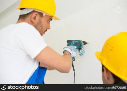 building, teamwork, working equipment and people concept - close up of builders with electric drill perforating wall indoors