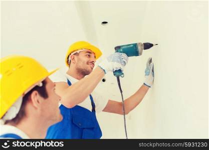 building, teamwork, working equipment and people concept - group of smiling builders s in hardhats with electric drill indoors