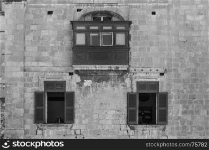 Building with traditional colorful maltese balcony in historical part of Valletta. Three red windows on the facade of a house in Malta. Black and white picture