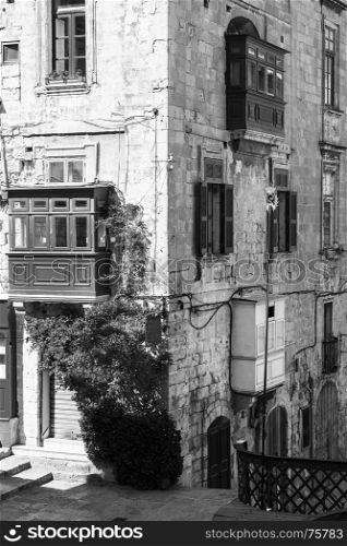 Building with traditional colorful maltese balcony in historical part of Valletta. Red windows decoreted with begonville on the facade of a house in Malta. Black and white picture