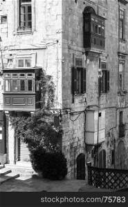 Building with traditional colorful maltese balcony in historical part of Valletta. Red windows decoreted with begonville on the facade of a house in Malta. Black and white picture