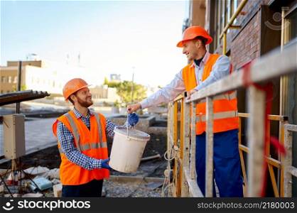 Building worker help each other at construction site. Builder deliver bucket with plaster to coworker. Builders help each other at construction site