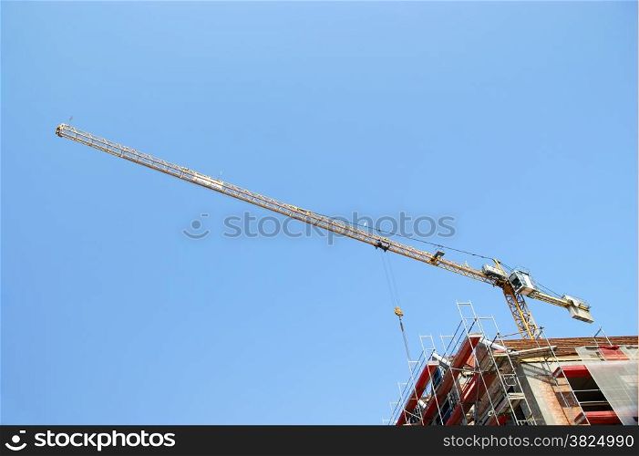 Building yellow tower crane in action against a blue sky