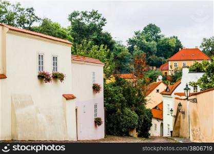 Buildings and houses in the historical center of Prague. Green trees, lamps, flowers in pot on the windows, red roofs