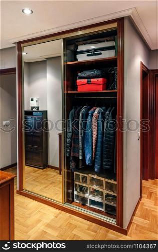Built-in wardrobe open with mirror doors in the corridor of an apartment. Built-in wardrobe open with mirror doors