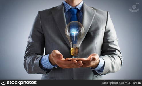 Bulb in hand. Businessman presenting glass glowing light bulb in his hand