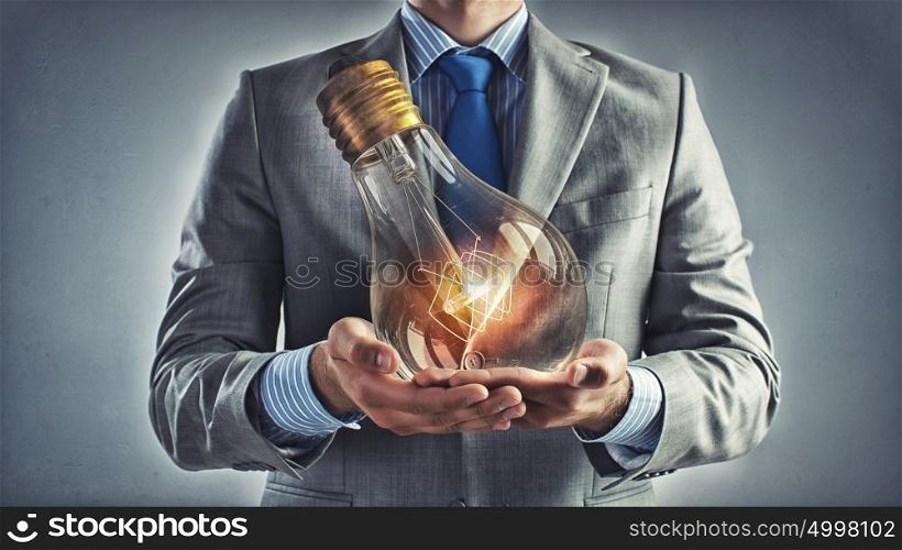 Bulb in hand. Young businessman presenting glass glowing light bulb in his hands
