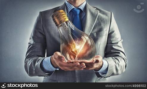 Bulb in hand. Young businessman presenting glass glowing light bulb in his hands