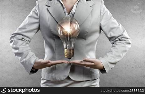 Bulb in hand. Young businesswoman presenting glass glowing light bulb in her hands