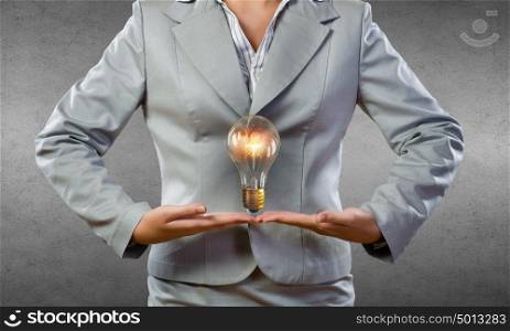 Bulb in hand. Young businesswoman presenting glass glowing light bulb in her hands