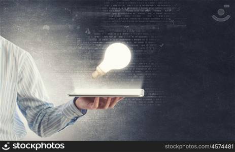 Bulb on tablet. Human hands holding tablet pc with light bulb on it
