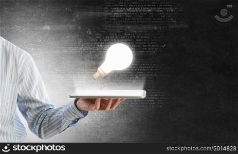 Bulb on tablet screen. Human hands holding tablet pc with light bulb on it