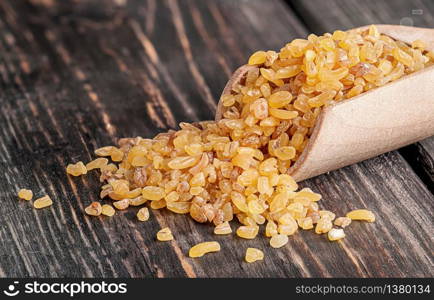 Bulgur in wooden scoop closeup on dark background. Bulgur in wooden scoop closeup