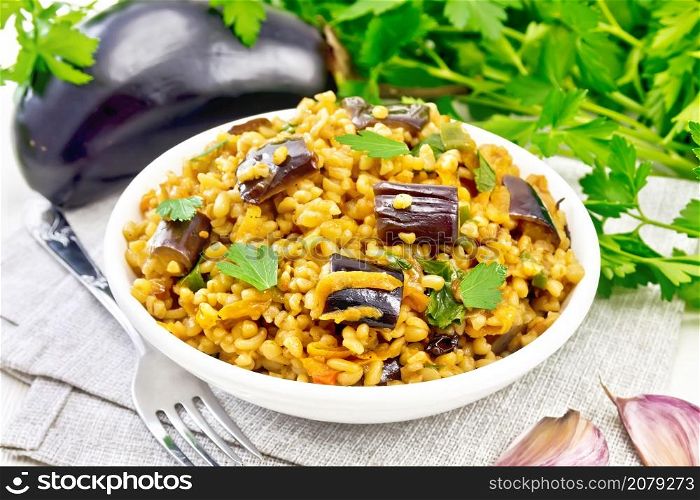 Bulgur stew with eggplant, carrots, garlic and onions in a bowl on a napkin on white wooden board background
