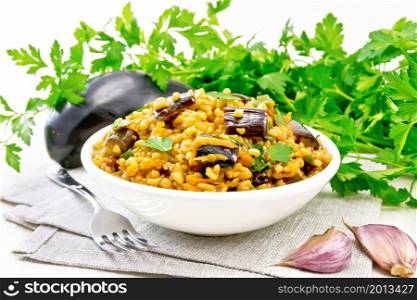 Bulgur stew with eggplants, carrots, garlic and onions in a bowl on a towel on wooden board background