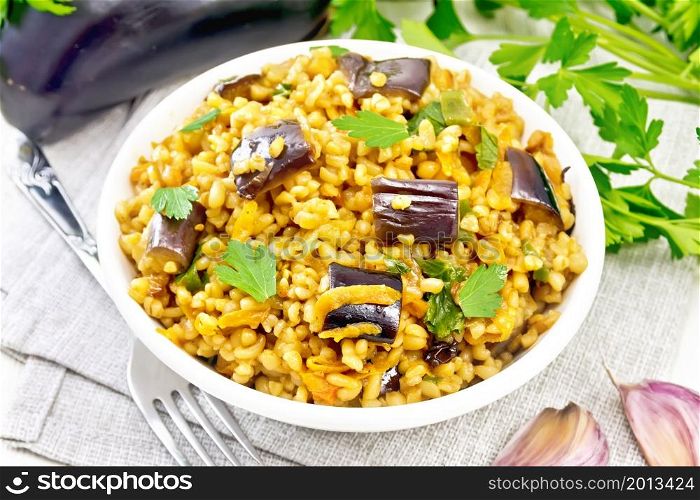Bulgur stewed with eggplants, carrots, garlic and onions in a bowl on a napkin on the background of light wooden board