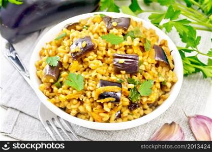 Bulgur stewed with eggplants, carrots, garlic and onions in a bowl on a napkin on the background of light wooden board