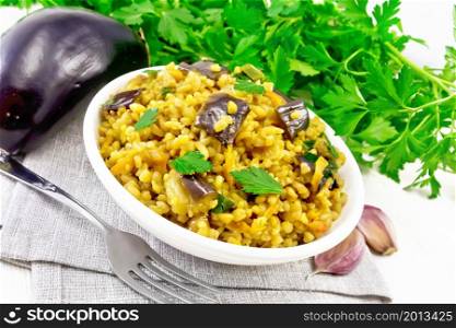 Bulgur stewed with eggplants, carrots, garlic and onions in a bowl on a napkin on wooden board background