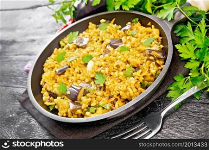 Bulgur stewed with eggplants, carrots, garlic and onions in a frying pan on a napkin on black wooden board background