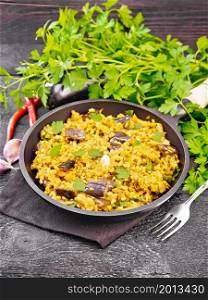 Bulgur stewed with eggplants, carrots, garlic and onions in a pan on a napkin on wooden board background