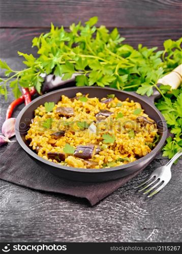 Bulgur stewed with eggplants, carrots, garlic and onions in a pan on a napkin on dark wooden board background