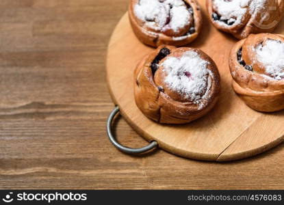 bun with currants covered with powdered sugar lay on a chopping board brown