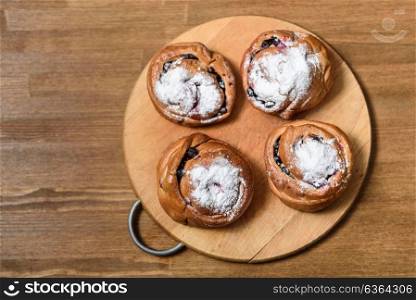 bun with currants covered with powdered sugar lay on a chopping board brown