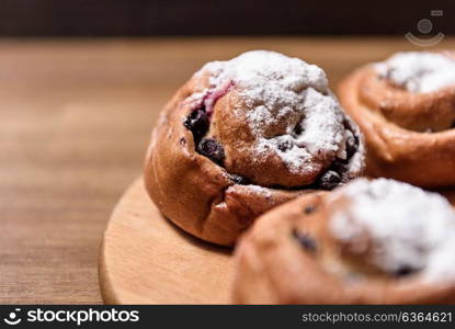 bun with currants covered with powdered sugar lay on a chopping board brown