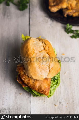 Bun with fried schnitzel and salad leaves on old wooden background, german tradition food