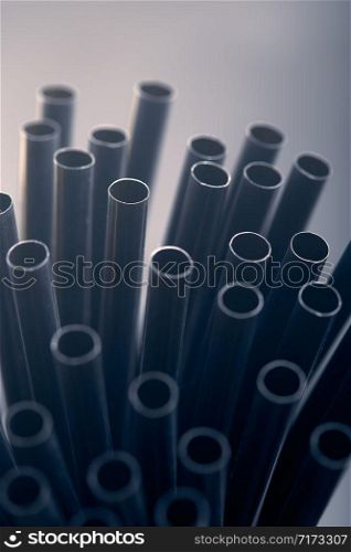 Bunch of black plastic straws scattered in container over plain grey background. Copy space for text
