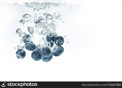 Bunch of blueberries splashing into crystal clear water and sinking under water with air bubbles background