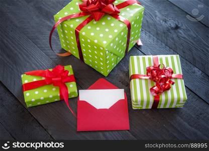Bunch of colorful presents, wrapped in paper and tied with red ribbon and bows, with an opened envelope and blank paper, on an old wooden table.