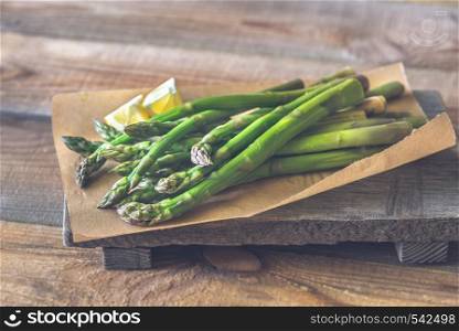 Bunch of cooked asparagus with lemon wedges on the wooden board