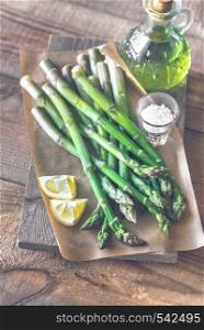 Bunch of cooked asparagus with lemon wedges, sea salt and olive oil on the wooden board