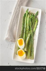 Bunch of cooked asparagus with soft-boiled egg on the white plate