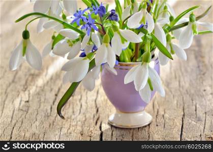 Bunch of Crocus and Snowdrops in a glass vase on old wooden table