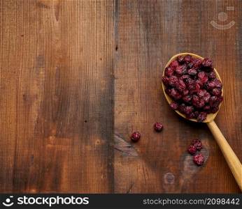 bunch of dried cranberries in a wooden spoon on a brown table. Delicious berry, top view