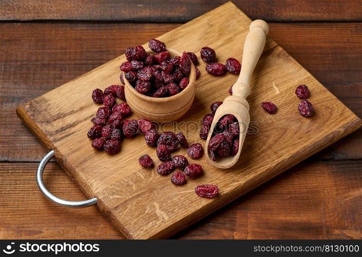 bunch of dried cranberries in a wooden spoon on a brown table. Delicious berry, top view
