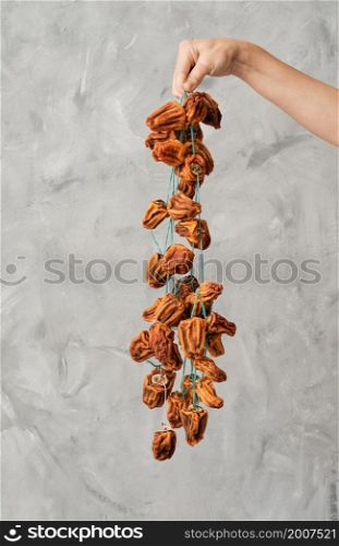 Bunch of dried persimmons is held in her hand by a girl, gray background. Dried persimmon, a traditional Japanese food dessert. Vertical frame, selective focus.