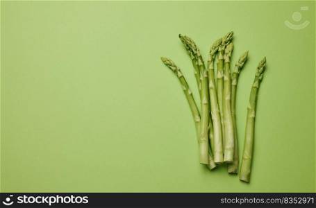 Bunch of fresh asparagus on green paper background, top view. Copy space