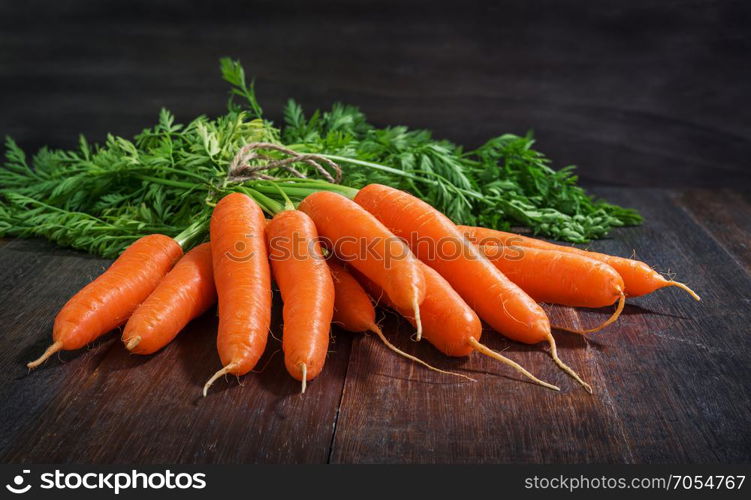 Bunch of fresh carrots vegetables with green leaves on rustic wooden background
