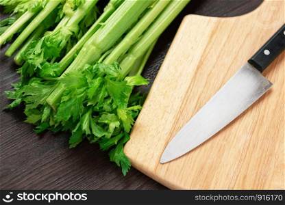 Bunch of fresh celery stalk on wooden table and cutting board and knife with leaves. Food and ingredients of healthy vegetable. Freshness herbal and low calories for dieting with plenty of vitamin